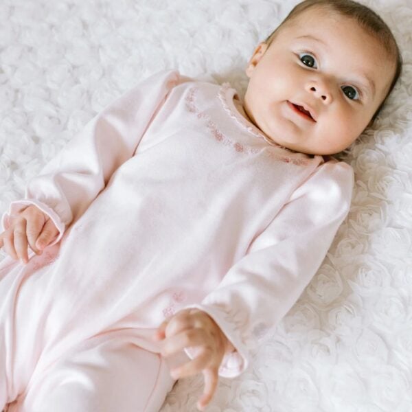 A gorgeous baby girls pink babygrow with a delicate lace edged neckline, which harmonises effortlessly with the lace on the ankles. Beautiful floral spray embroideries in shades of pink, sit just below the lace neck. Two more floral sprays curve where pockets would normally be and a matching pull on hat completes the set. A perfect new baby gift.