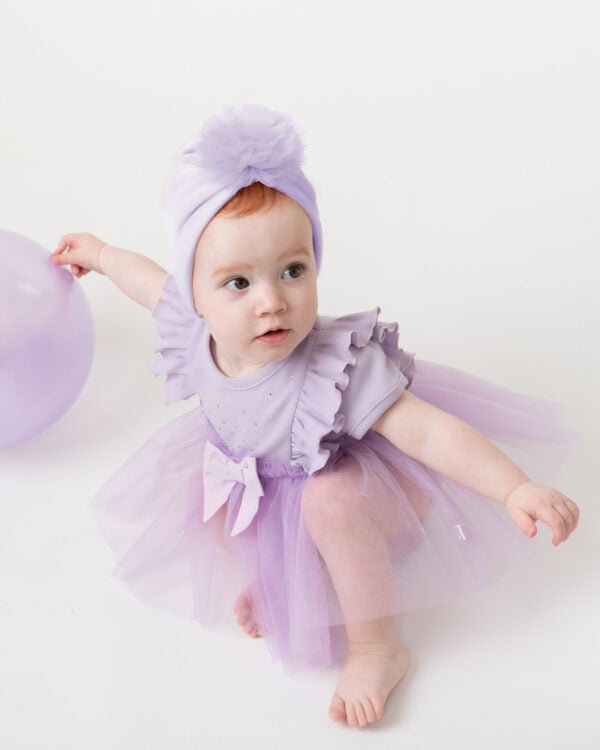 Lovely for a party, this lilac purple dress set for baby girls is by Caramelo Kids. The dress is made in soft cotton jersey, decorated with pretty ruffles, sparkly diamanté, and a fixed bow on the front. The gathered tulle skirt has attached jersey knickers which fasten with poppers between the legs. The dress comes with a matching turban style hat to complete the party look.